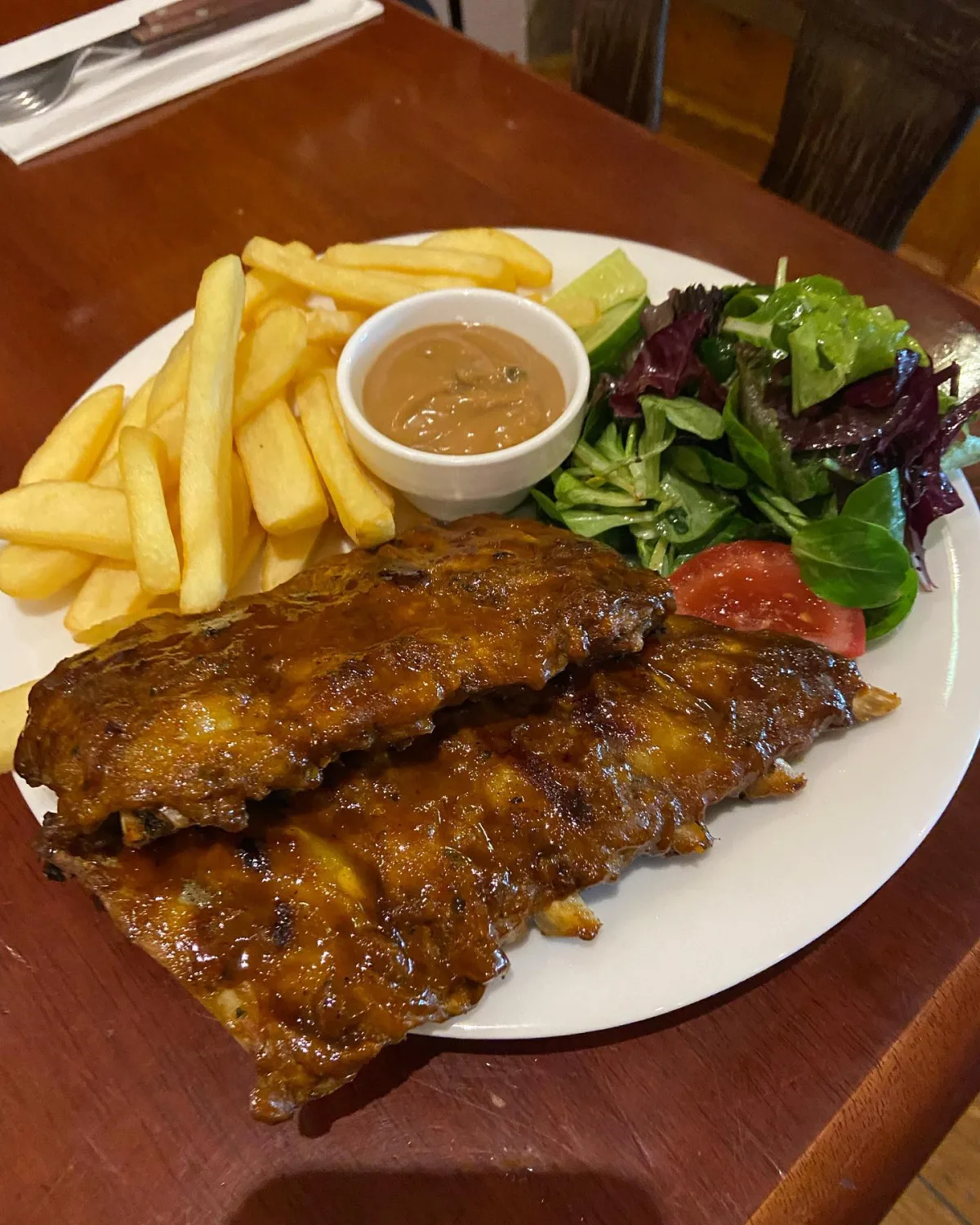 Spareribs van de grill met friet, salade en een kuipje saus op een wit bord