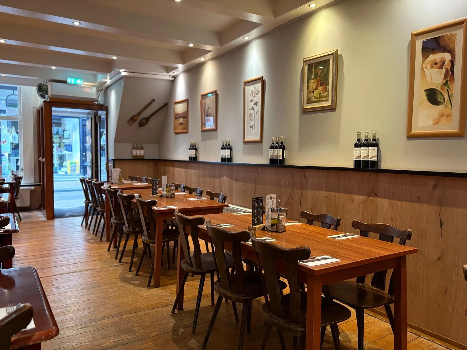 Gedekte tafels met houten stoelen in het restaurant, met wijnflessen en schilderijen aan de wand