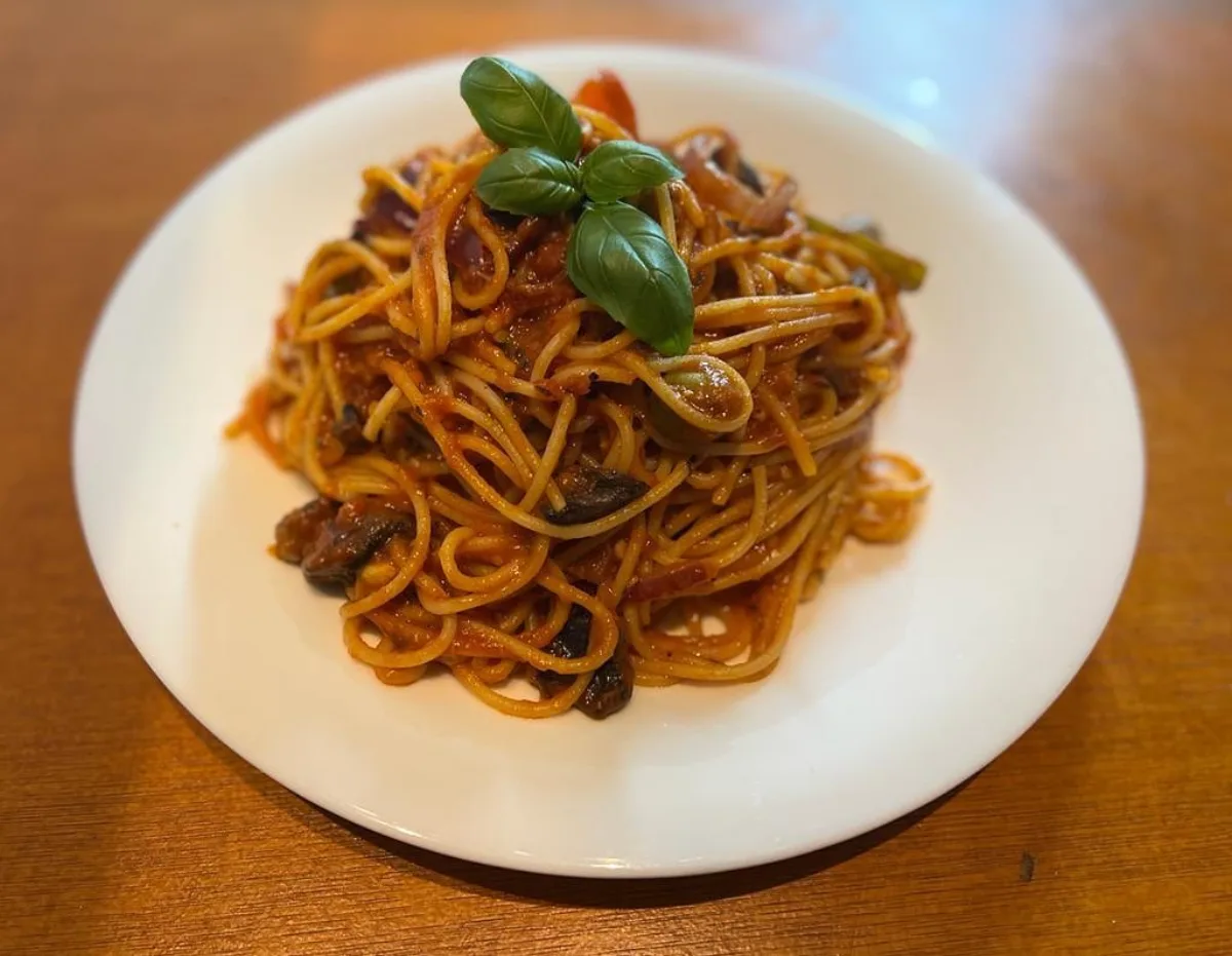 Bord spaghetti met tomatensaus, olijven en verse basilicum, op een houten tafel